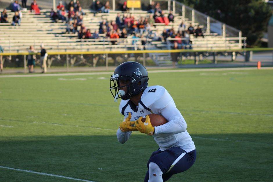 Football player in uniform runs during a game at a sunny outdoor stadium with audience.